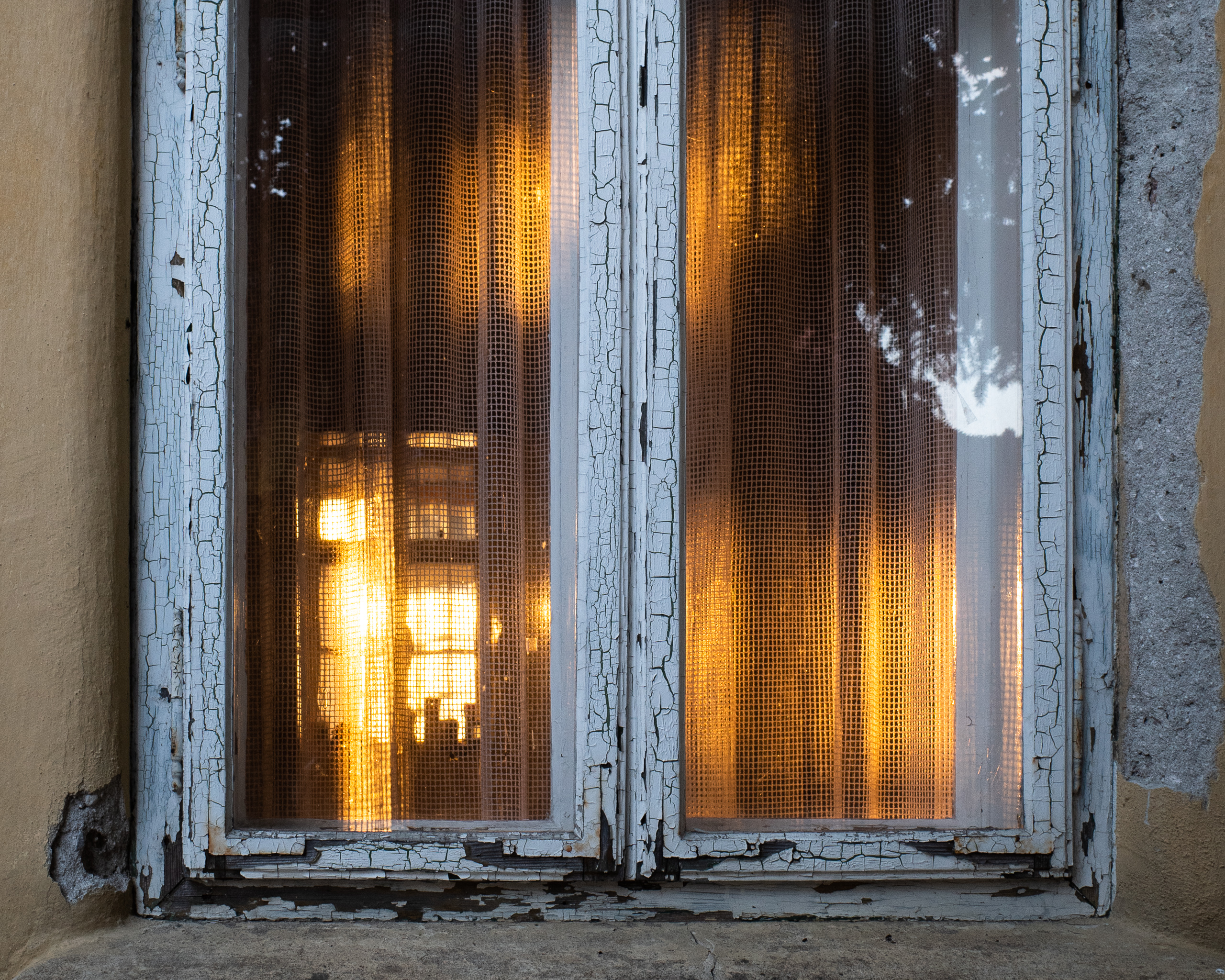 Abendsonne hinter der Gardine – am Fensterrahmen blättert die Farbe